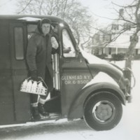 Milkman with a full bottle carrier in his hand, standing in the door of his delivery truck on a snowy day, c.1950s.jpg