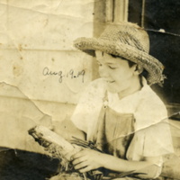 Leon A. Rushmore, Jr. in straw hat and overalls, shucking an ear of corn at Rushmore Farms, Aug. 1918.jpg